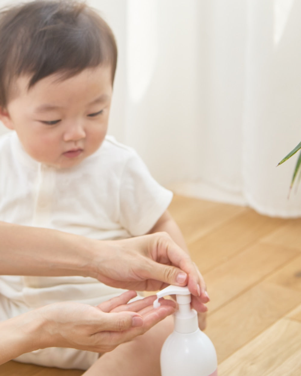 赤ちゃんのそばでボディミルクを手に取るママ
